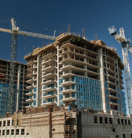 White crane towers at a large construction site with condominium balconies against a blue sky
